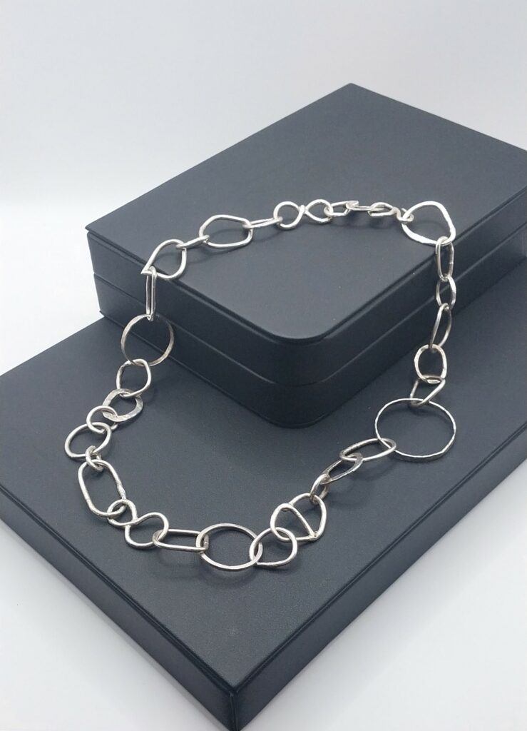 handmade sterling silver necklace with individually unique links displayed on a stand