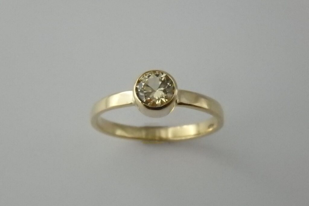 A closeup of a handmade ring in 18karat gold with a simple, plain band and a round yellow sapphire gemstone in a bezel setting.