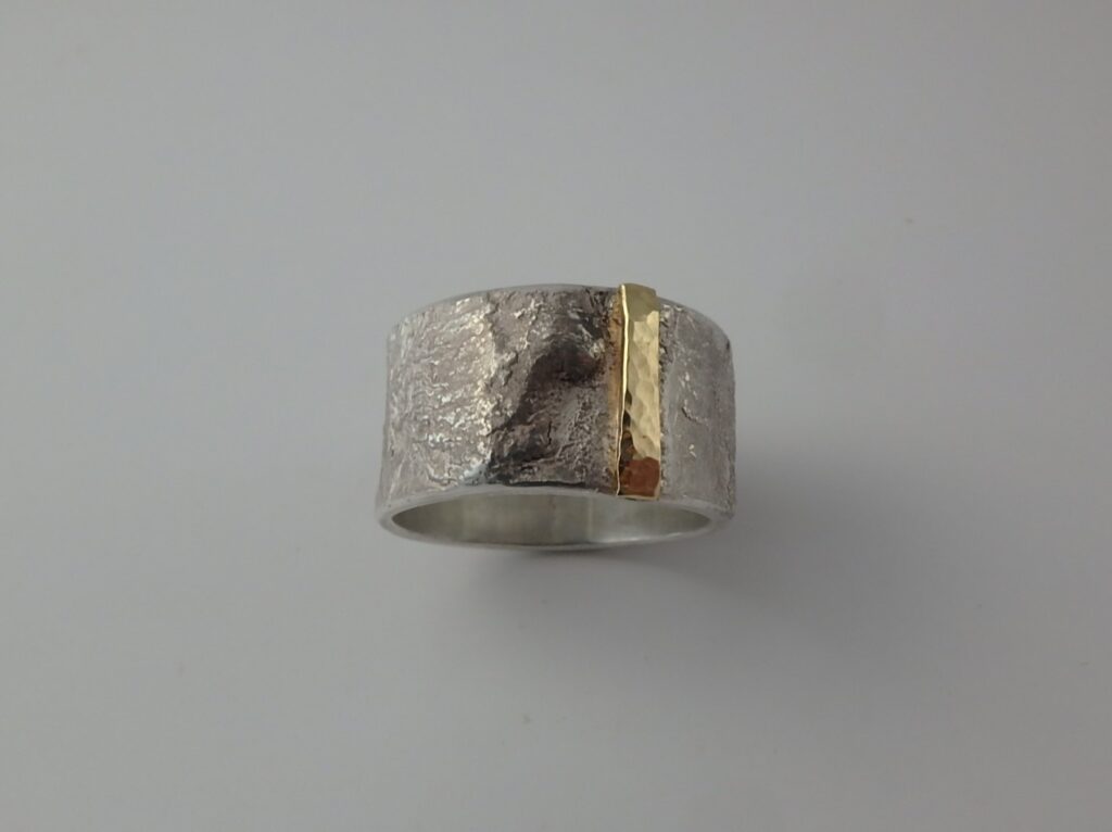 A wide sterling silver band ring with surface texturing and a thick strip of 18karat yellow gold highlight.