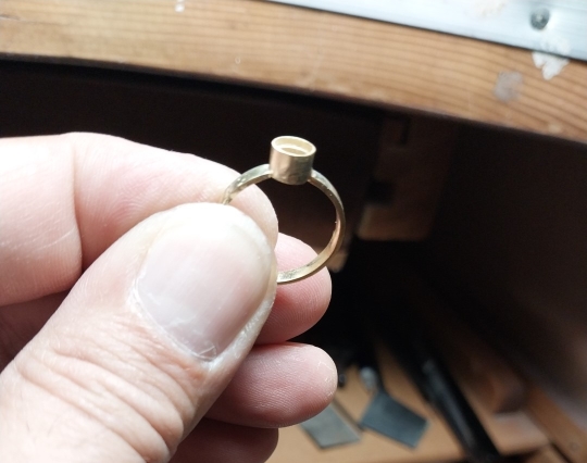 An 18karat gold ring being held to show that it is fully assembled but does not yet have a stone set in it.